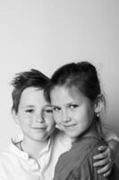 Black and white studio portrait of a young boy and girl standing side by side, holding hands, full-body shot with soft lighting and a clean background. Calm and tender mood. photo