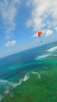 Cinematic FPV drone shot of paragliders gliding over cliffs and turquoise ocean at Pandawa Beach, Bali. Aerial view of dramatic coastline, tropical waves, and summer sky video