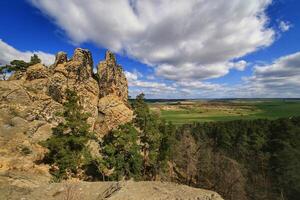 Sandstone spires stand above forested slopes and open farmland beneath rolling clouds photo