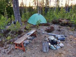 Campfire tent setup in forest clearing with wooden bench and rocky fire ring nearby photo