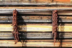 Rusted chains hang from a wooden cabin wall, casting long shadows in the morning light photo