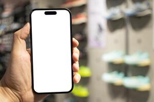 Hand Holding Blank Smartphone in Shoe Store. Mobile shopping for footwear, using retail apps, comparing prices online, or showcasing digital advertisements. photo
