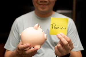 Man Holding Pension Note and Piggy Bank. A smiling man holds a piggy bank and a yellow sticky note with Pension text. saving for retirement and future financial security. photo