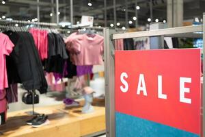 Red Sale Sign in Clothing Store. discounts and promotions on apparel. Racks of various clothes are visible in the background. shopping discounts, consumerism and promotions. photo