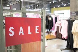 Red Sale Sign in Clothing Store. discounts and promotions on apparel. Racks of various clothes are visible in the background. shopping discounts, consumerism. photo