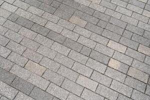 Textured grey paving stones laid in a diagonal pattern, creating a durable and classic outdoor surface. The rough texture and varying shades of grey. photo