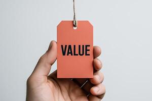 Hand holding orange tag with value text and string, branding and marketing concept, price label, worth perception and business communication photo