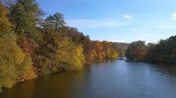 Beautiful autumn scenery. Calm blue river surrounded with yellow, red and orange tree under blue sky. Panoramic view. video