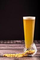 Tall glass of cold beer with frothy head beside spilled peanuts on wooden surface with black background. Concept of bar snack, beer pairing and casual pub moment. Glass of beer with peanuts on wood photo