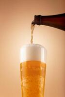 Golden beer pours from bottle into tall glass, creating thick foam and visible bubbles. Warm gradient background adds sense of refreshment and movement. Beer foam rising in tall glass photo