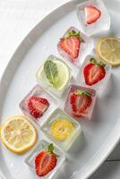 Refreshing Fruit Ice Cubes on White Plate with Strawberries, Lemon, Lime and Mint photo