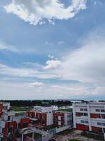 Aerial view of urban buildings with red and white facades merging into green fields and a river beneath a partly cloudy sky. Ideal for cityscape, nature, and landscape themes. photo