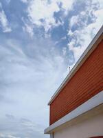 Low angle shot of red brick building corner with white trim against a blue sky and scattered clouds. Strong architectural lines and contrast. Ideal for urban and design themes. photo