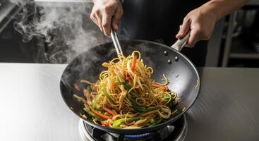 Chef hands tossing steaming vegetable stir fry noodles in a hot wok on a stove photo