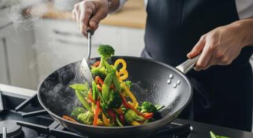 Chef hands stir frying vibrant vegetables in a wok with rising steam photo