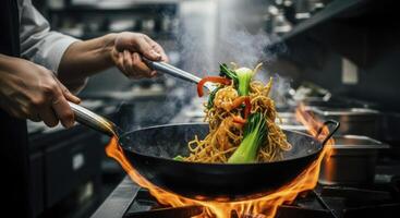 Professional chef stir frying asian noodles with vegetables and shrimp in a flaming wok photo