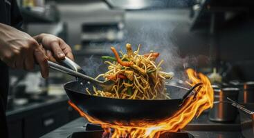 Professional chef rapidly tossing stir fried noodles in a sizzling wok with high flames photo