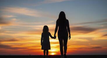 Silhouette of mother and daughter holding hands walking towards sunset sky photo