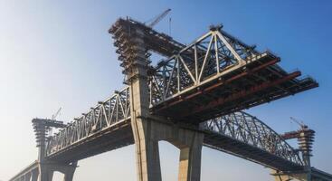 Massive modern bridge under construction with steel truss framework and concrete pylons against blue sky photo