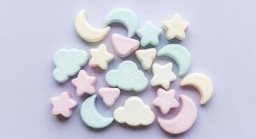 Pastel colored marshmallows in star, moon, and cloud shapes scattered on a light surface photo