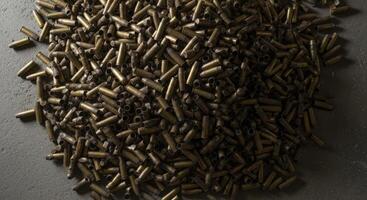 Chaotic pile of spent brass shell casings, some tarnished and gleaming, on a dark surface photo