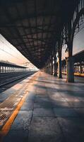 Empty train station platform at dusk with shadows stretching out along the concrete floor creating an eerie yet peaceful atmosphere photo