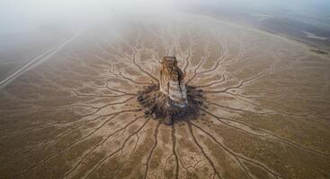 Majestic rock formation stands tall amidst cracked earth patterns creating an otherworldly desolate desert landscape photo