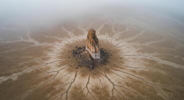 Mystical rock formation rising from a cracked desert floor shrouded in fog creates a dramatic earthy landscape photo