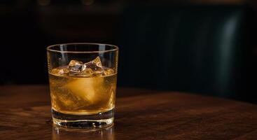 A glass of whisky with ice cubes rests on a wood table offering a sophisticated drink concept for menus and promotions photo