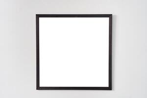 An empty square photo frame with a black border hanging on a white wall