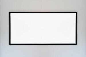 An empty photo frame with a black border hanging on a white wall