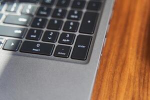 Top view of a part of a gray laptop keyboard on a wooden table photo