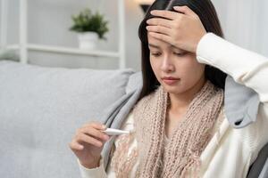 Young Asian woman having high fever while checking body temperature, female sneezing and runny nose with seasonal influenza, allergic, digital thermometer, virus, coronavirus, illness photo