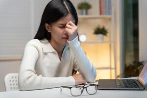 Eye problems, Asian women with tired and irritated eyes, eye rubbing, dry, eye pain after work, migraine, headache, blurred vision, photophobia, working in the dark, blue light from computer screen. photo