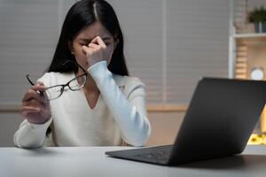 Eye problems. Asian women with tired and irritated eyes, eye rubbing, dry, eye pain after work, migraine, headache, blurred vision, photophobia, working in the dark, blue light from computer screens photo