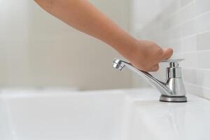 Little kid hand closed the faucet at sink in house with mom. Mother teaches child to save water. keeps turning off the water to save world energy and protect the environment. photo