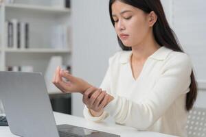 Asian young woman working in office with a carpal tunnel syndrome or wrist joint inflammation, hand muscle inflammation from office syndrome , hand muscle pain from work. photo
