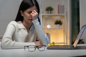 Eye problems, Asian women with tired and irritated eyes, eye rubbing, dry, eye pain after work, migraine, headache, blurred vision, photophobia, working in the dark. blue light from computer screen. photo