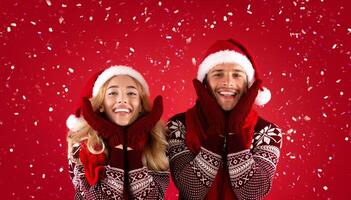 It's Christmas time. Adorable young couple in mittens, Santa hats and scarves on red background photo