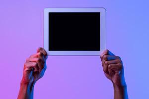 Hands Of African American Man Holding Digital Tablet With Black Blank Screen, Showing Free Copy Space For Your App Or Website Design, Standing In Neon Lighting Over Purple Studio Background, Mockup photo