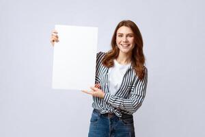 Cheerful Young Woman With Blank Placard In Hands Standing Over Light Gray Studio Background. Positive Millennial Lady Demonstrating Empty Billboard With Copy Space For Your Text And Advertisement photo