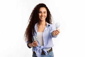 Smiling Lady Showing Compact Fluorescent Lamp Light Bulb To Camera Standing Over White Studio Background. Lightbulbs Disposal Service, Choose Energy-Saving Light-Bulb Concept photo