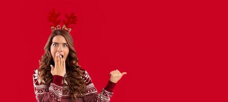 Christmas sale. Shocked millennial woman pointing at blank space over red background, panorama photo