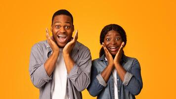 Great Offer. Amazed African American Couple Touching Cheeks In Excitement, Happy Black Lovers Emotionally Reacting To Nice Surprise, Standing Together Isolated Over Yellow Background, Free Space photo
