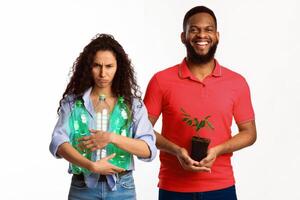 Don't Litter And Care For Nature. Smiling Man Holding Green Plant While Discontented Woman Holds Wasted Plastic Bottles Standing On White Background. Studio Shot. Environment And Ecology Protection photo