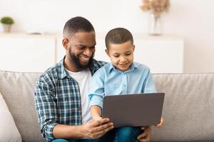 Little Boy Watching Movie On Tablet Sitting On Dad's Knees, Using Computer Together And Browsing Internet At Home. Gadgets, Weekend Family Leisure Concept photo