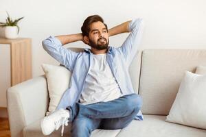 Domestic Rest. Portrait Of Smiling Arab Man Leaning Back On Sofa With Hands Behind Head, Happy Millennial Eastern Man Relaxing On Comfortable Couch In Living Room At Home, Free Space photo