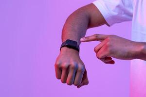 African Male Using Smartwatch With Black Blank Screen, Unrecognizable Man Checking Time Or Physical Activity, Standing In Neon Lighting Over Purple Background, Panorama With Copy Space, Mockup photo