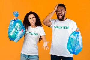 Don't Litter. Two Angry Volunteers Man And Woman Shouting Holding Blue Garbage Bags Posing Over Yellow Studio Background. Volunteering Work, Stop Using Plastic Concept photo
