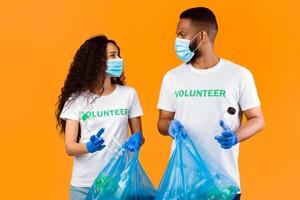 Two Diverse Volunteers Holding Plastic Bottles And Bags With Litter Working Picking Garbage Standing In Studio On Yellow Background. Waste Sorting And Disposal. Keep Environment Clean Concept photo